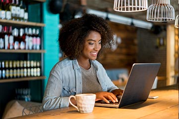 Smiling woman in coffee shop uses screen sharing to collaborate from her laptop