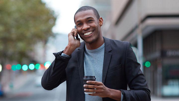 Uomo sorridente al telefono che cammina per strada