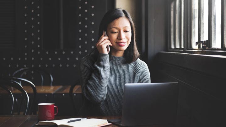 Kvinde på telefonen sidder ned med sin bærbare computer